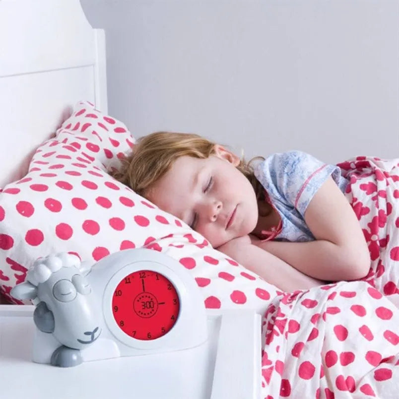 Child sleeping in a bed with red polka dot bedding next to a red alarm clock.